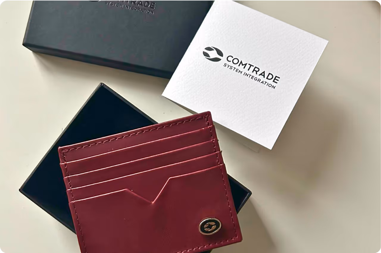 Luxury red leather wallet in a black box with Comtrade System Integration branding card on a light background.