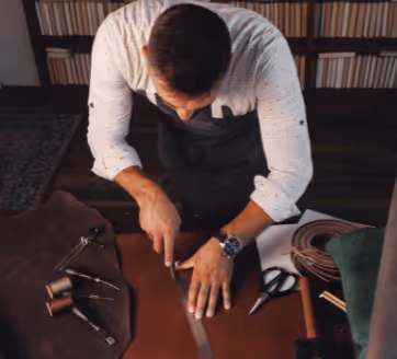 A man in an apron is cutting a piece of wood.