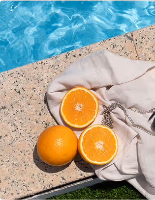 A pair of sunglasses and an orange on a towel next to a pool.