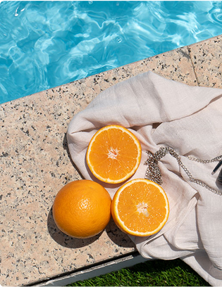 A pair of sunglasses and an orange on a towel next to a pool.
