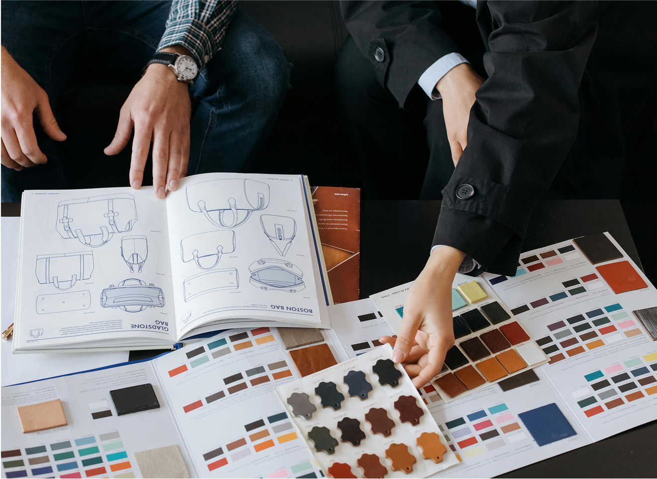 Two people reviewing design sketches and leather color samples on a table during a creative meeting."