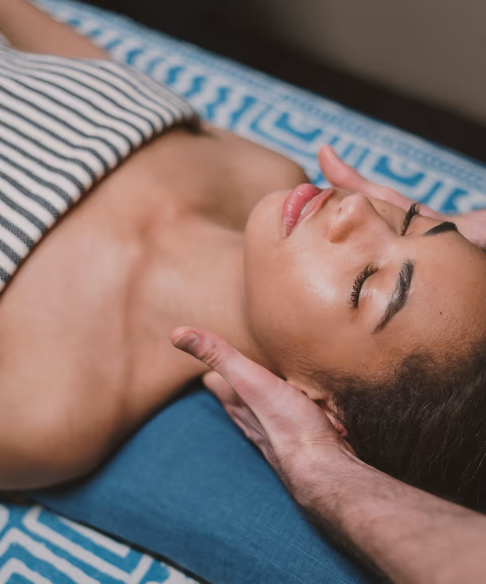 Vrouw ligt ontspannen met gesloten ogen tijdens een gezichtsmassage op een blauw-gepatroonde tafel bij schoonheidssalon in Limburg