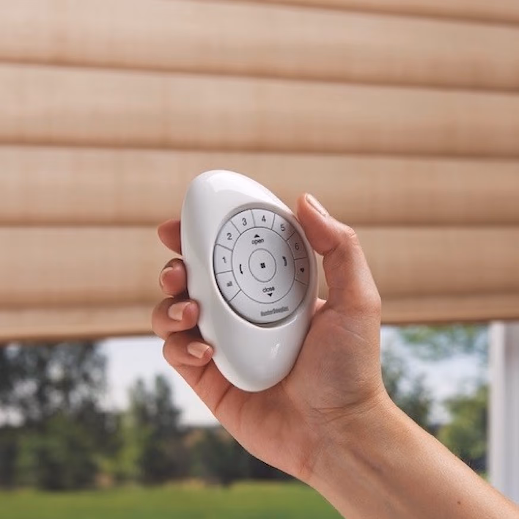 A hand holding a remote control for motorised blinds, allowing easy adjustment of window coverings for improved accessibility and comfort.