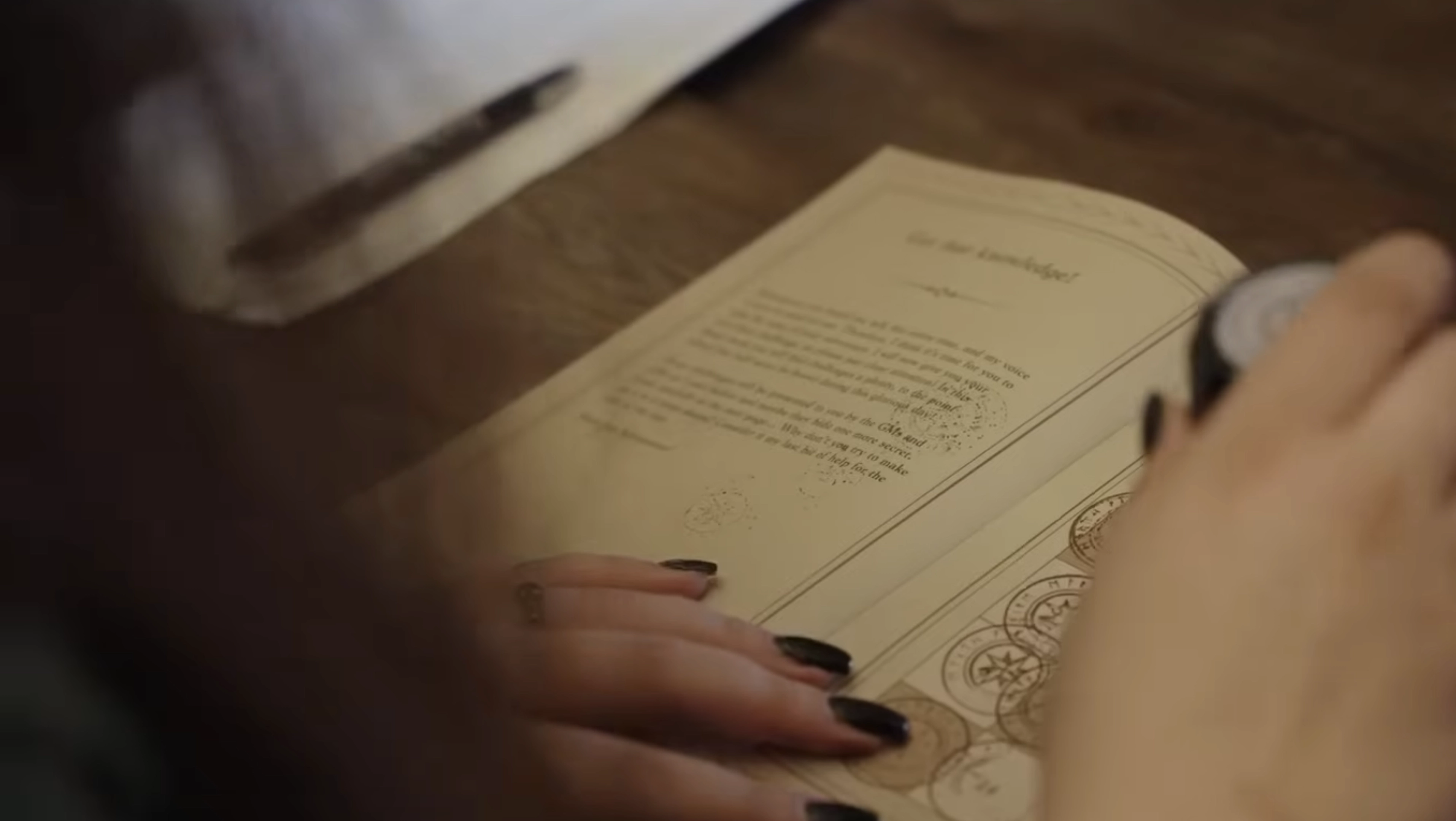 Image showcasing a scene from a video shoot through the lens of a camera. Two women and one man are looking at a magazine on the table, while the rest of the image is blurred