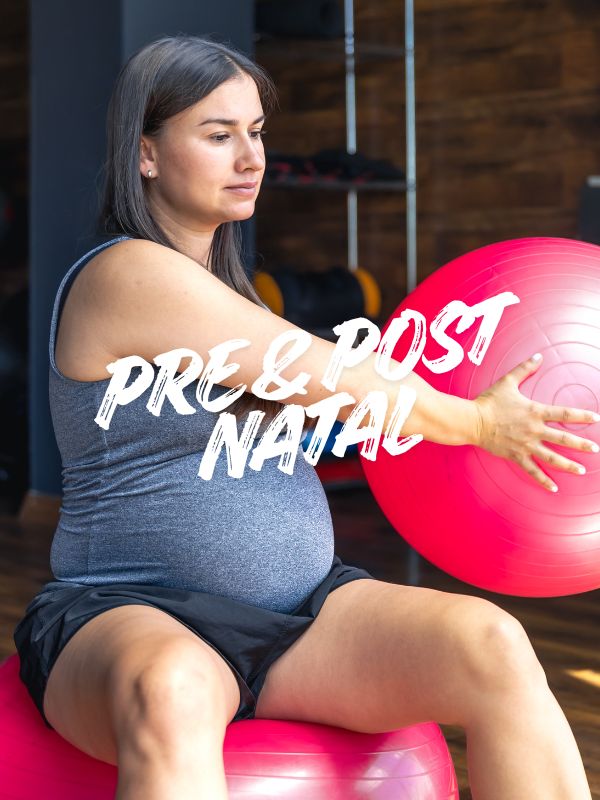 Woman in purple shirt doing overhead dumbbell press with assistance from a trainer in a gym.