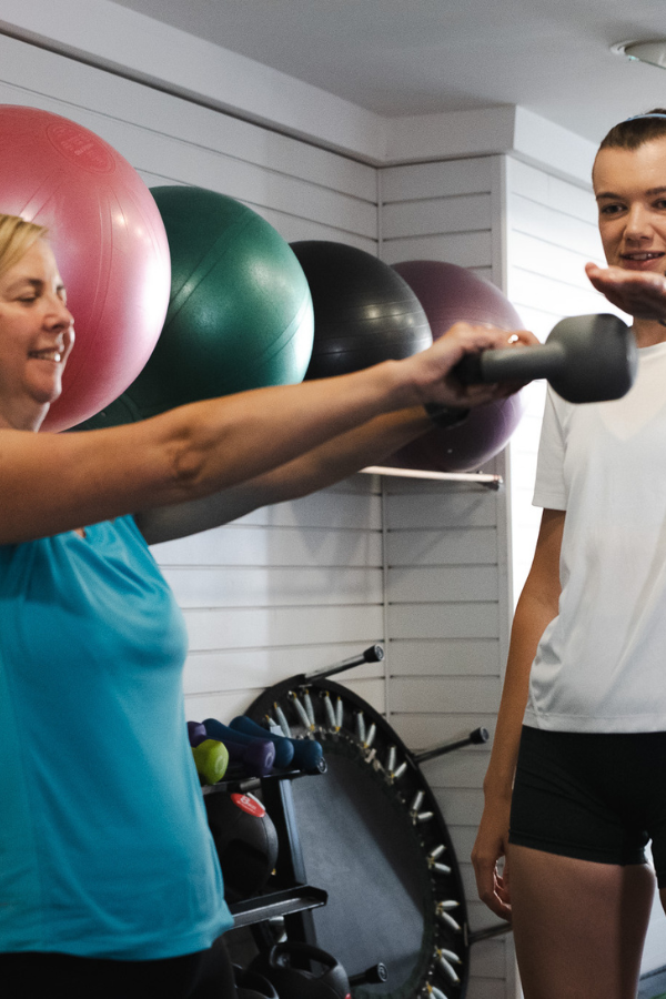Woman in a hoodie exercising legs on a leg curl machine in a gym.