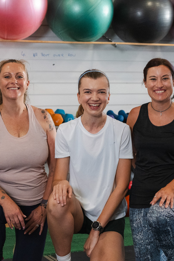 Smiling woman in a blue shirt using gym cable machine with rope attachment.