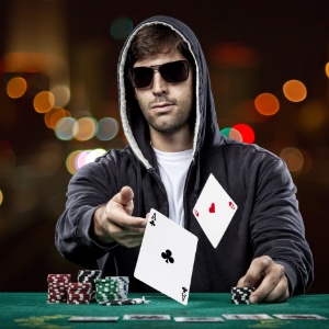 A nan sitting at a poker table flicking two aces towards the front