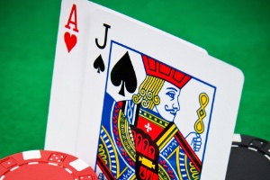 A close up of a black jack of spades and ace of hearts wurrounded by poker chips on a green felt background 