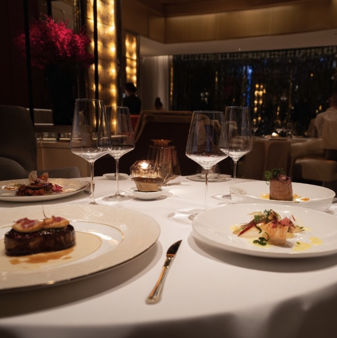 A close up image of a white table clothed dining table set in a restaurant with fine dining meals on the table and wine glasses