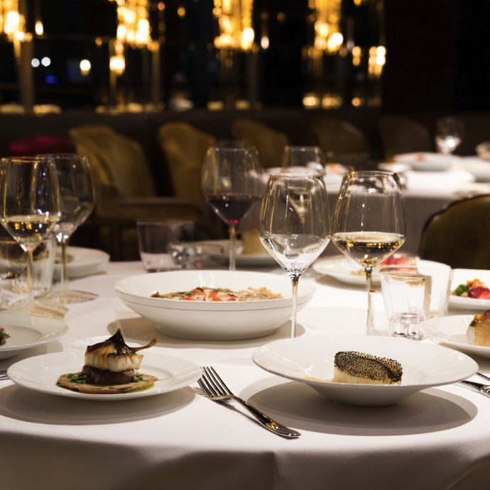 Set in a fine dining restaurant with a table full of fine dining meals on a crisp white table cloth and wine glasses