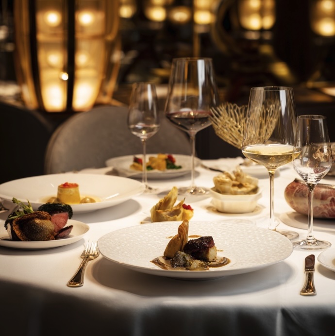A restaurant setting with a close up of a white table clothed dining table covered in fine dining dishes and wine glasses