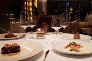 A close up image of a white table clothed dining table set in a restaurant with fine dining meals on the table and wine glasses