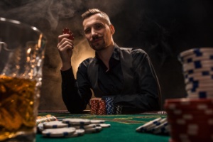 A man wearing a black shirt sitting at a poker table surrounded by cigar smoke and poker chips