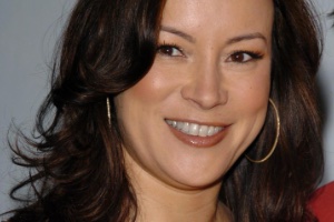A close up image of Jennifer Tilly with her hair and makeup done and wearing gold hoop earrings