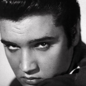 An image of a man dressed similar to Elvis singing at an event with International written on the curtain behind him