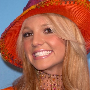An image of Britney Spears close up smiling at an event wearing an orange and purple hat and jewelled necklace