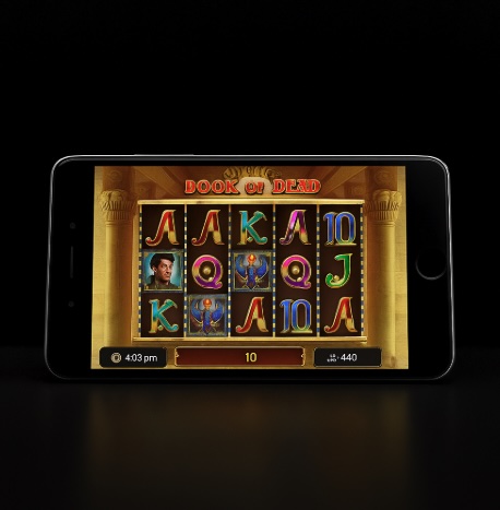 An image of a mobile phone on a black background with an image similar to the BOOK OF DEAD slot game on the screen