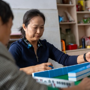 An image of a lady sitting at home playing Mahjong with family or friends