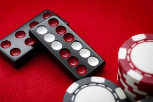 A close up image of red, white and black dominoes and red, black and white poker chips on a red felt background