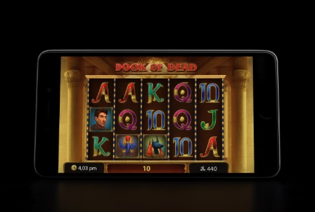 An image of a mobile on a black background with the slot game similar to Book of Dead on the screen