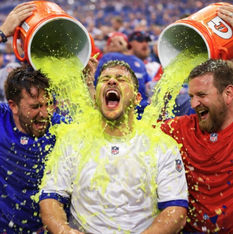 An image of two men pouring  liquid similar to Gatorade over the man in the centre at an event like the Super Bowl