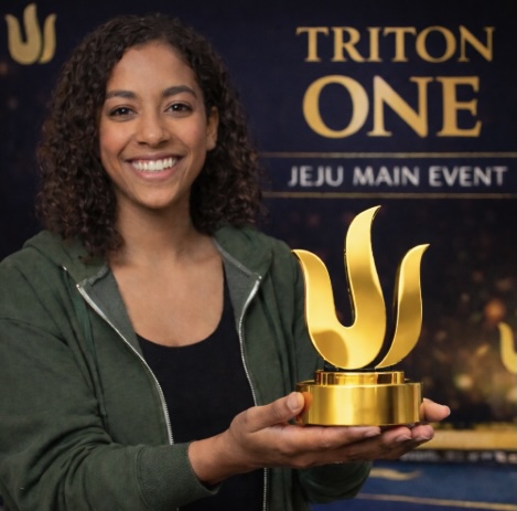 An image of a woman standing at an event similar to the Triton One Jeju Main Event holding a gold trophy