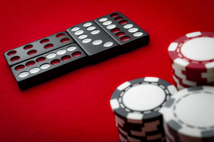 An image of a red felt top poker table with 4 dominoes and 3 stacks of poker chips in red, white and black on it