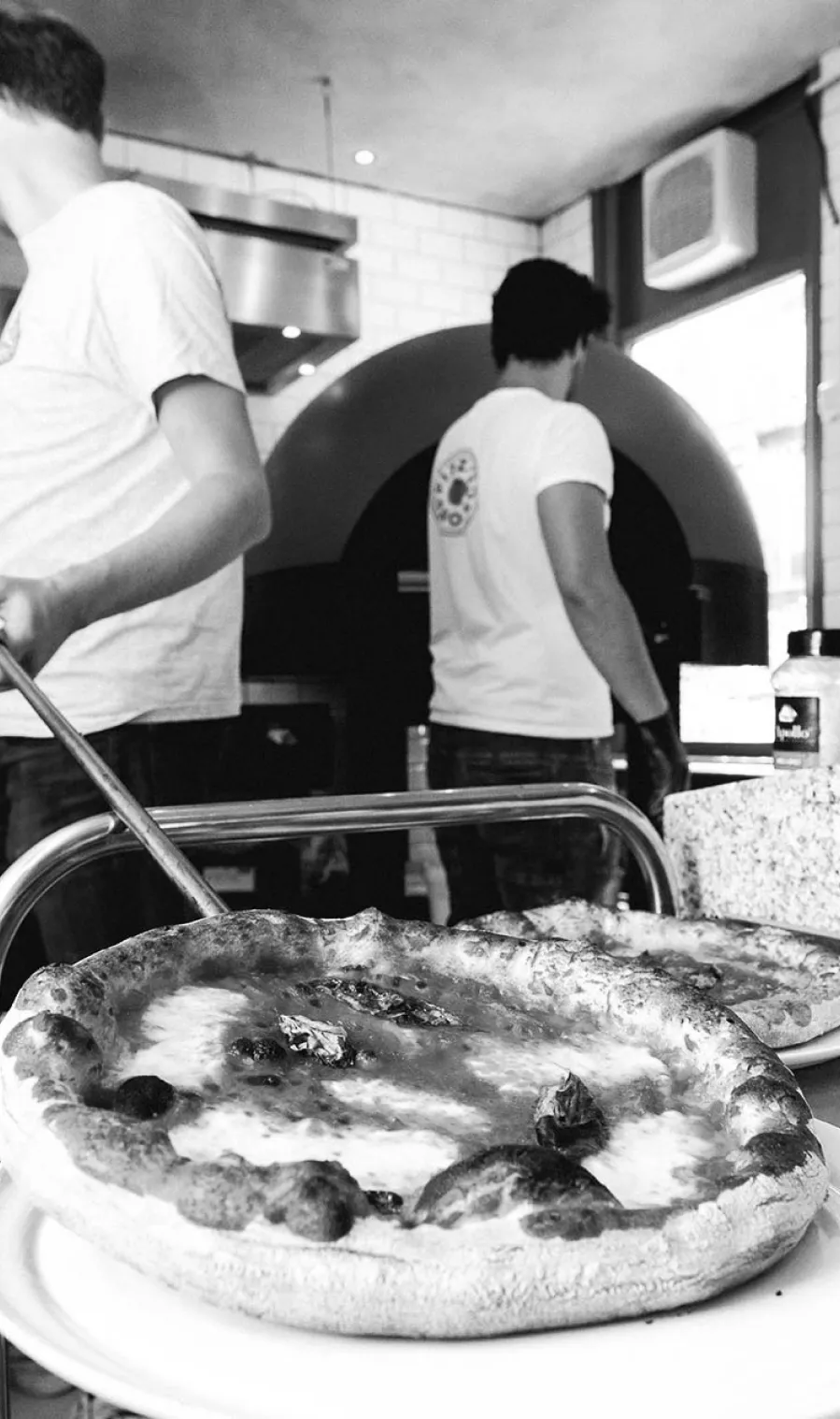 Two guys busy in the kitchen preparing pizza