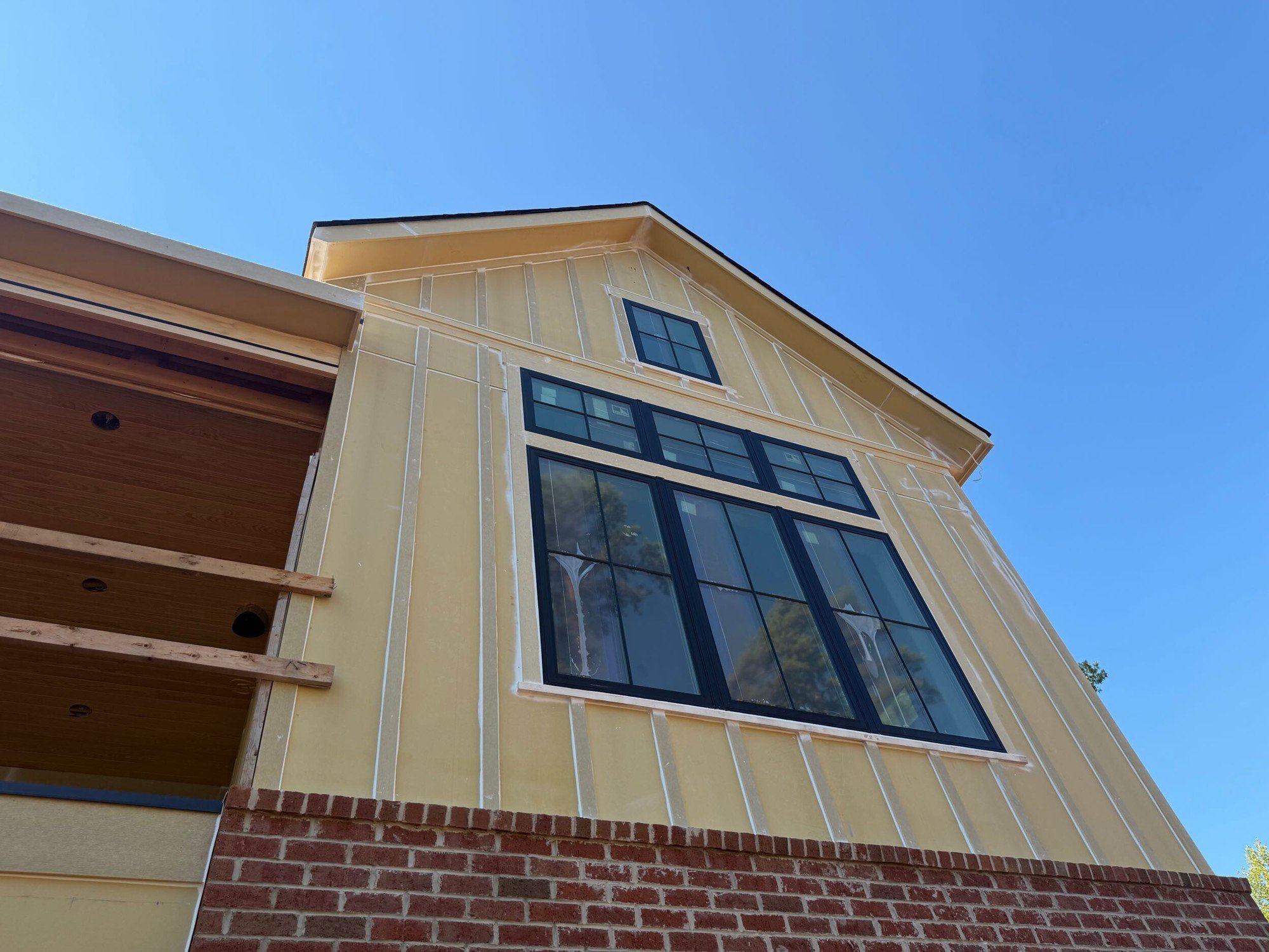 Board-and-batten siding and a large black-framed window above red brick on a gable of a home under construction in McLean, Clover SC.