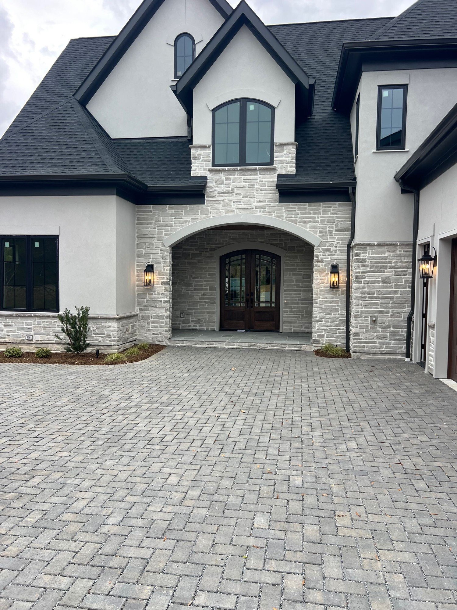 Arched stone entry with double wood doors and a paver drive at a finished home in Montreaux, Charlotte NC.
