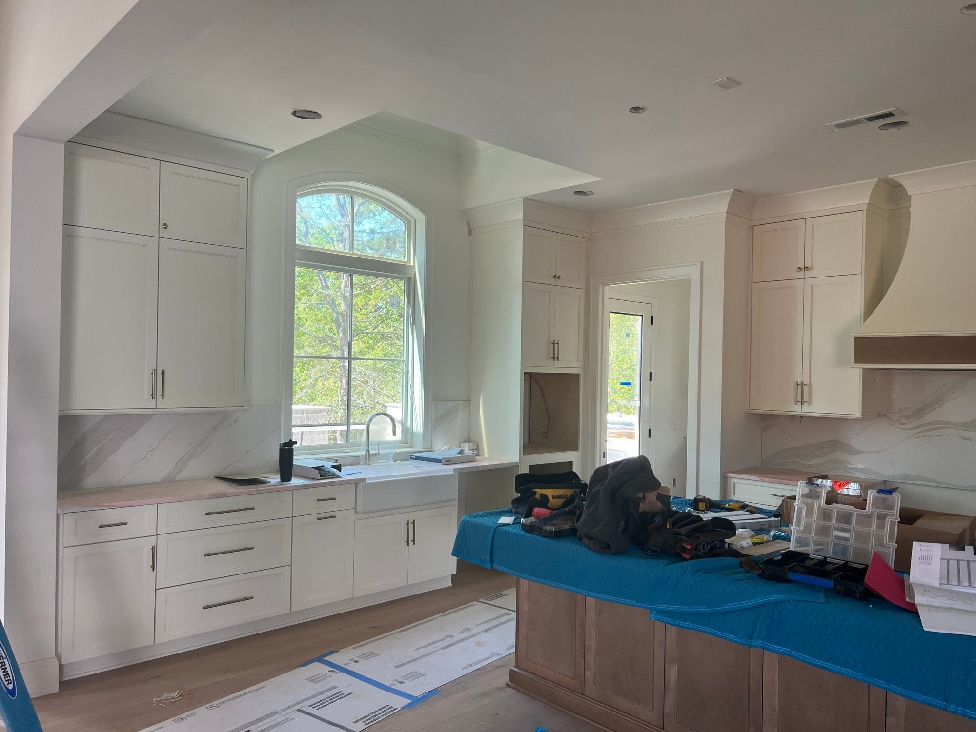 A white kitchen with an arched window, painted cabinets and a stained wood island covered for protection.