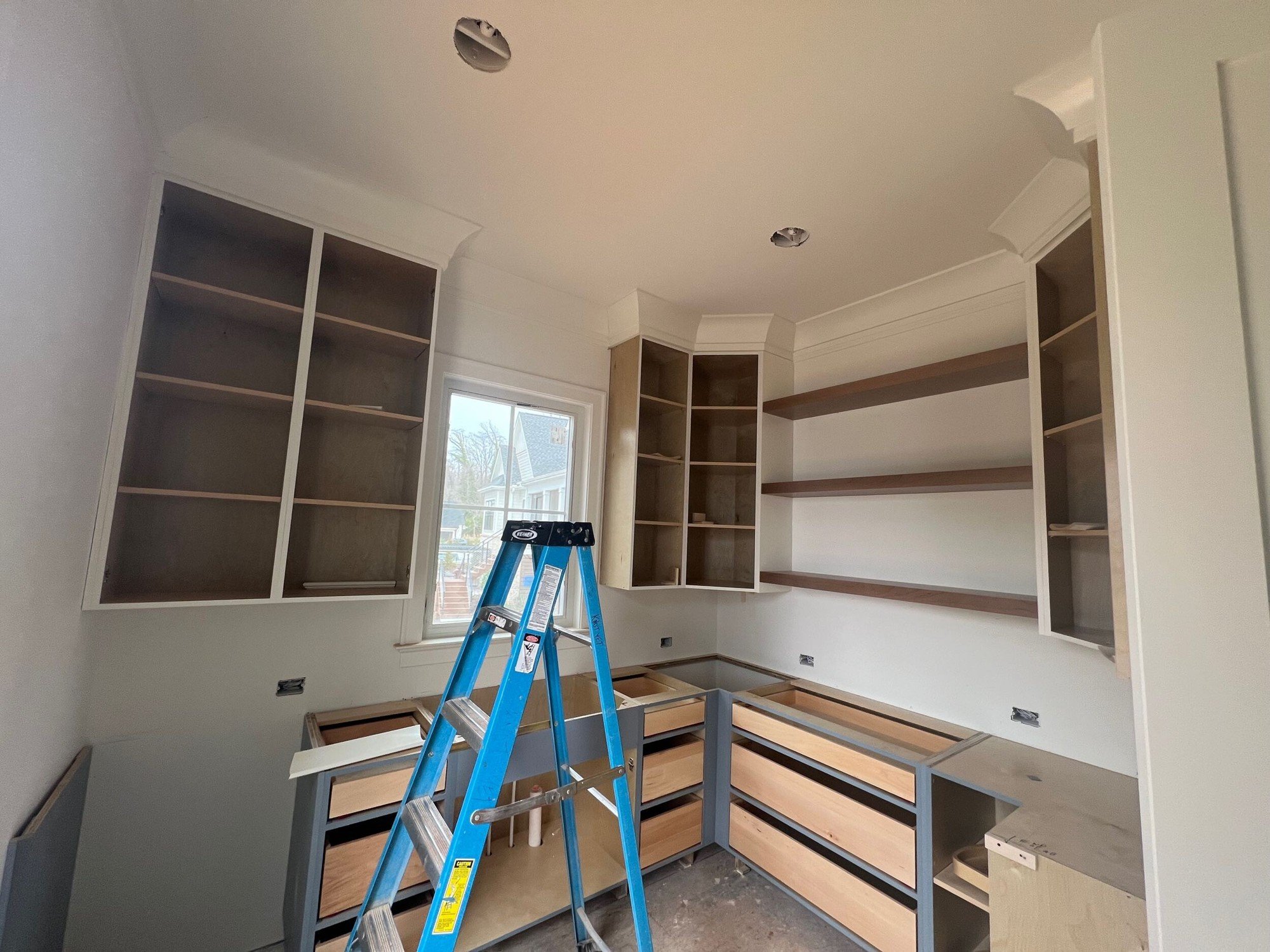 Cabinet boxes and open shelving installed in a kitchen corner, with a stepladder in front.