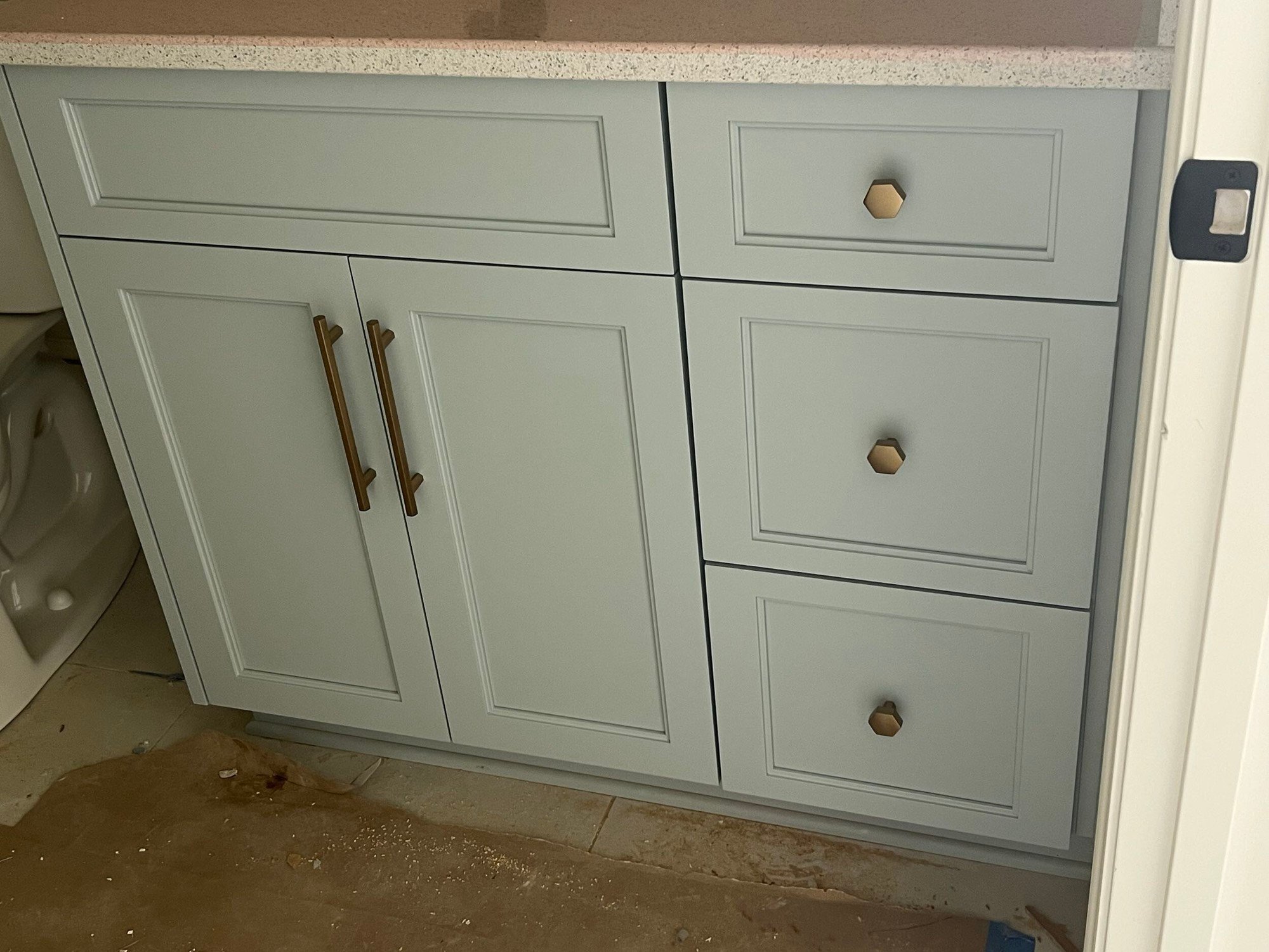 Sage green vanity cabinet with brass knobs and pulls.