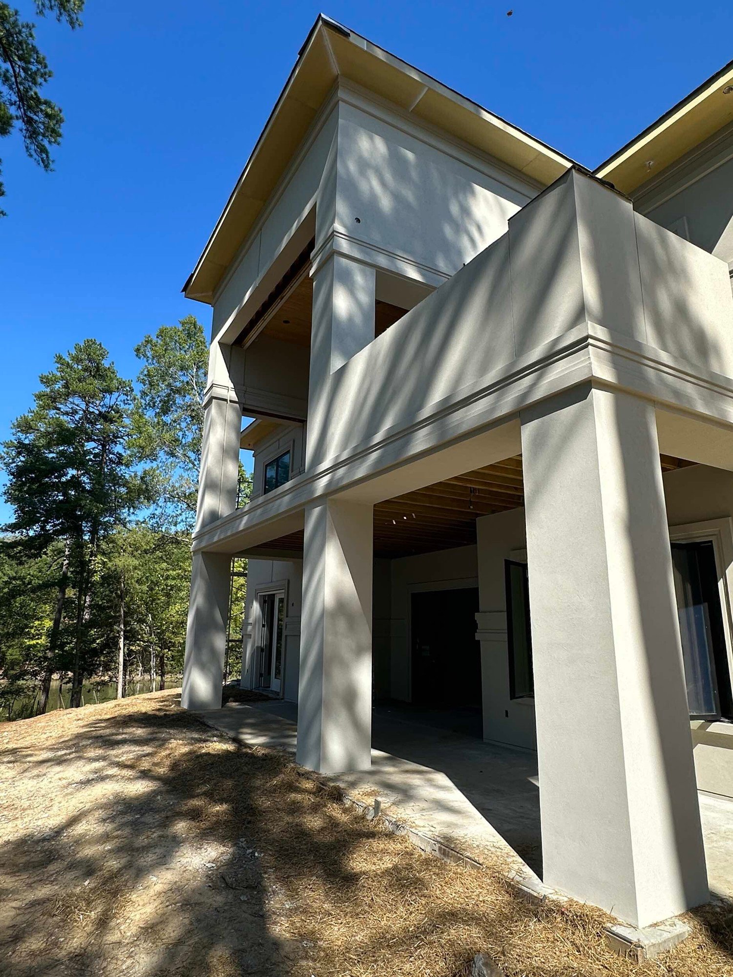 Stucco columns under an upper deck with a wood porch ceiling, set among pine trees.