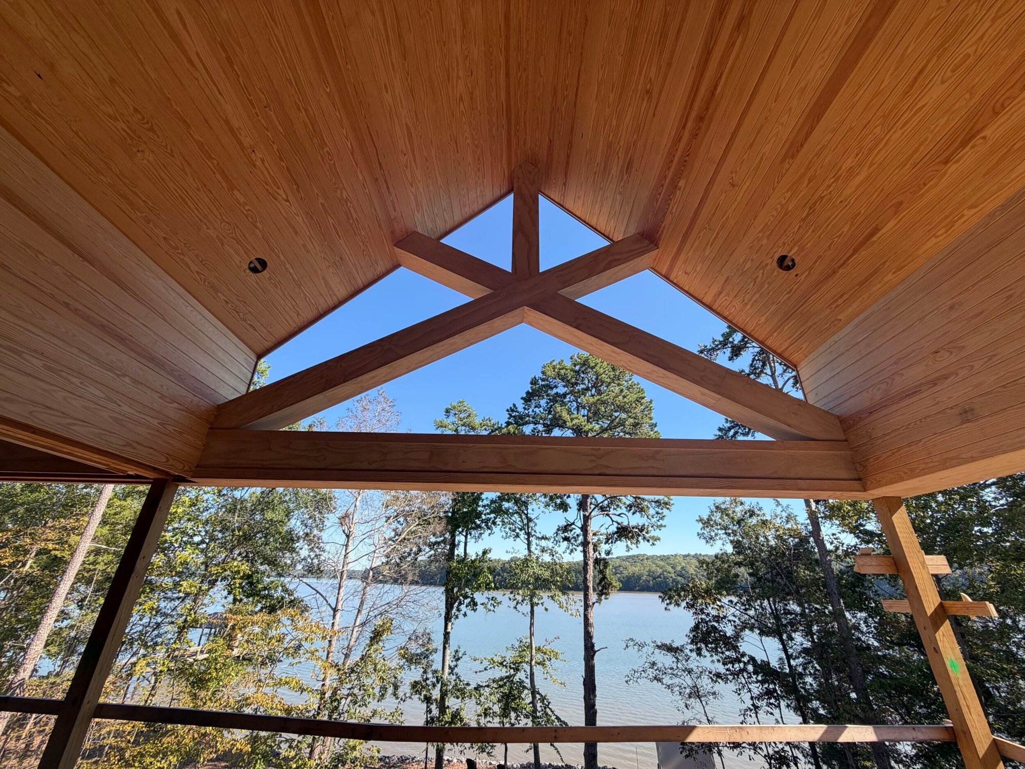 Pine ceiling and dark timber trusses framing a view of the lake through the trees.