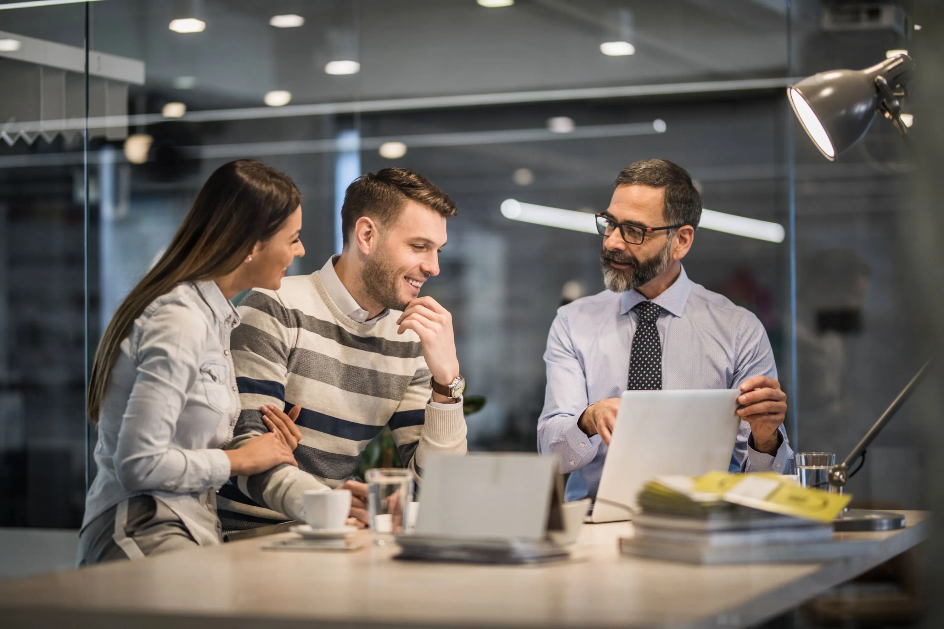 Three colleagues discussing work together in a modern office, one holding a laptop.