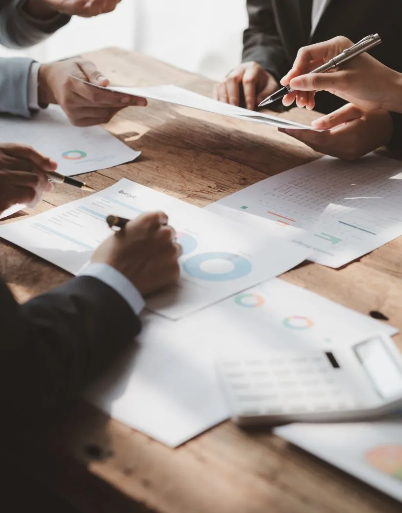 People reviewing and discussing business charts and graphs at a wooden table with pens and a calculator.