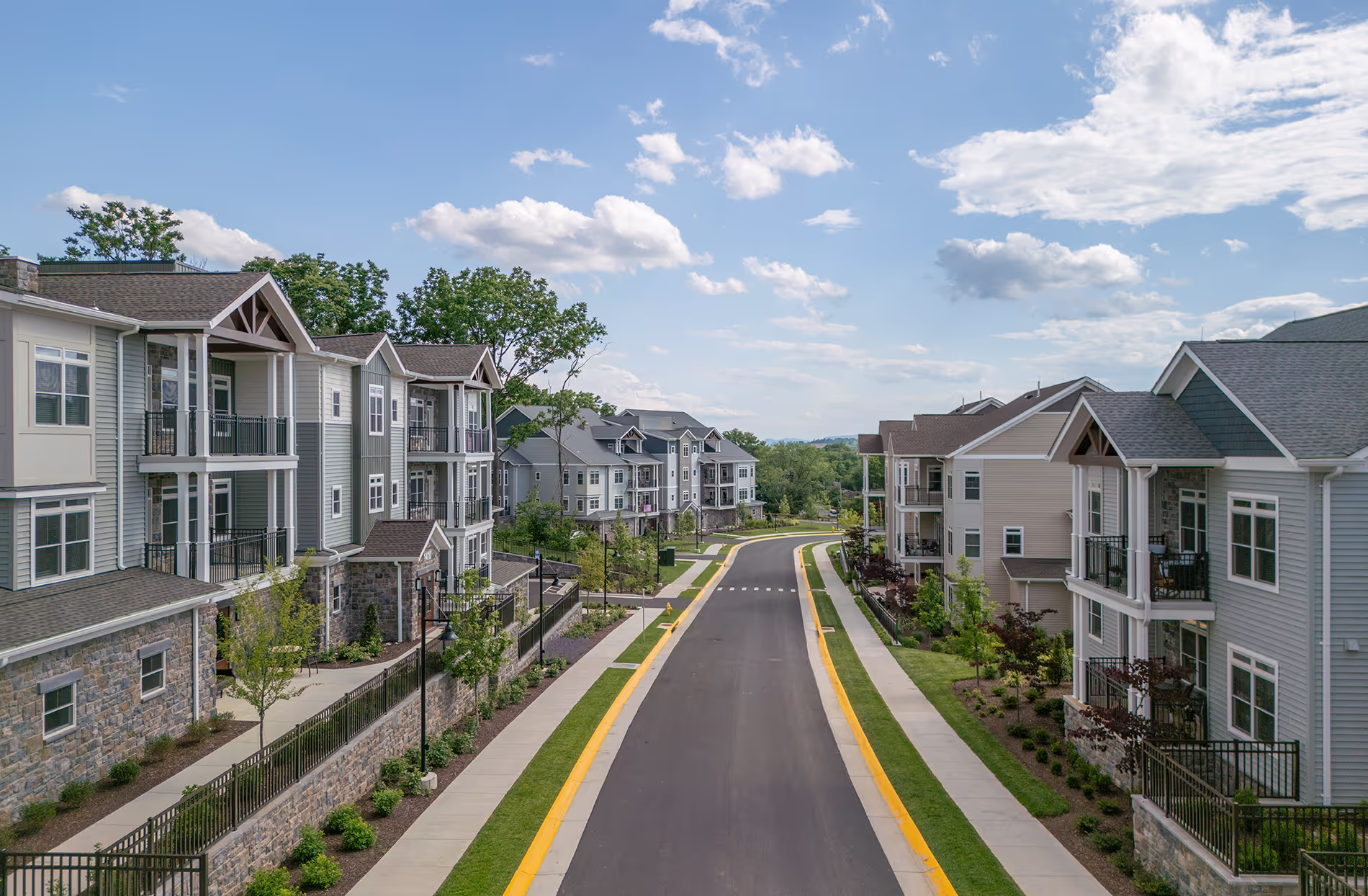 Residential street with modern apartment buildings and clear skies. Sidewalks and trees line the road.
