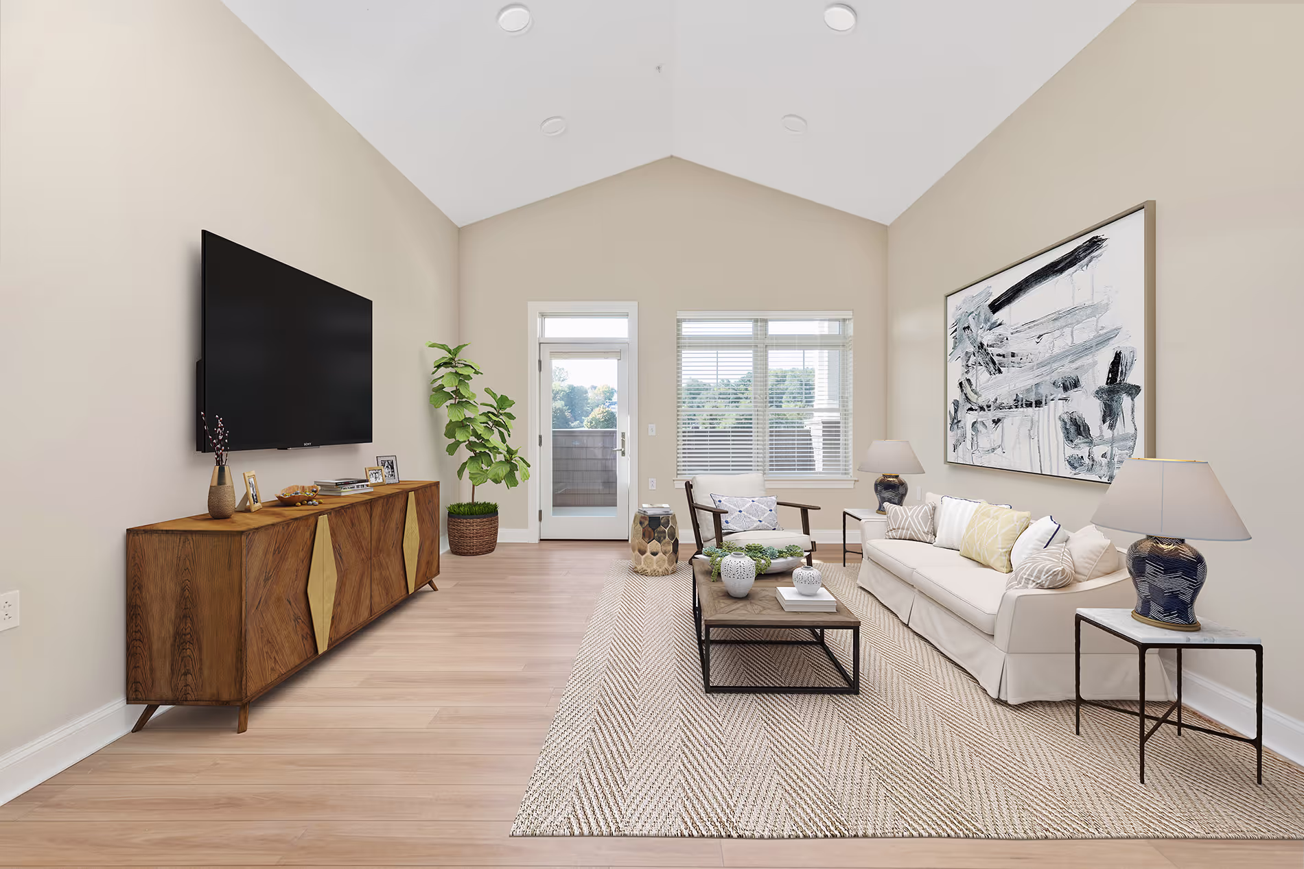 A bright living room with a sofa, large wall-mounted TV, and modern wooden cabinet.