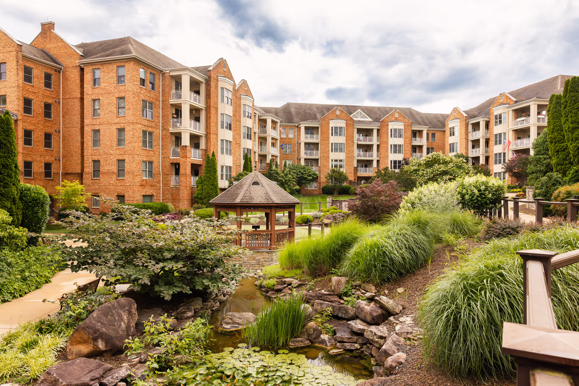 A landscaped garden with a wooden gazebo sits in front of a large brick apartment building.