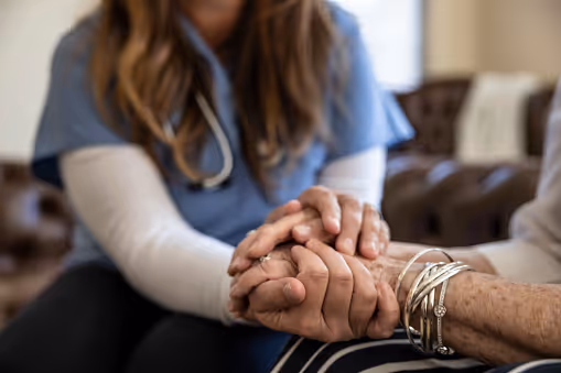 A nurse gently holds a patient's hand, providing comfort and support.