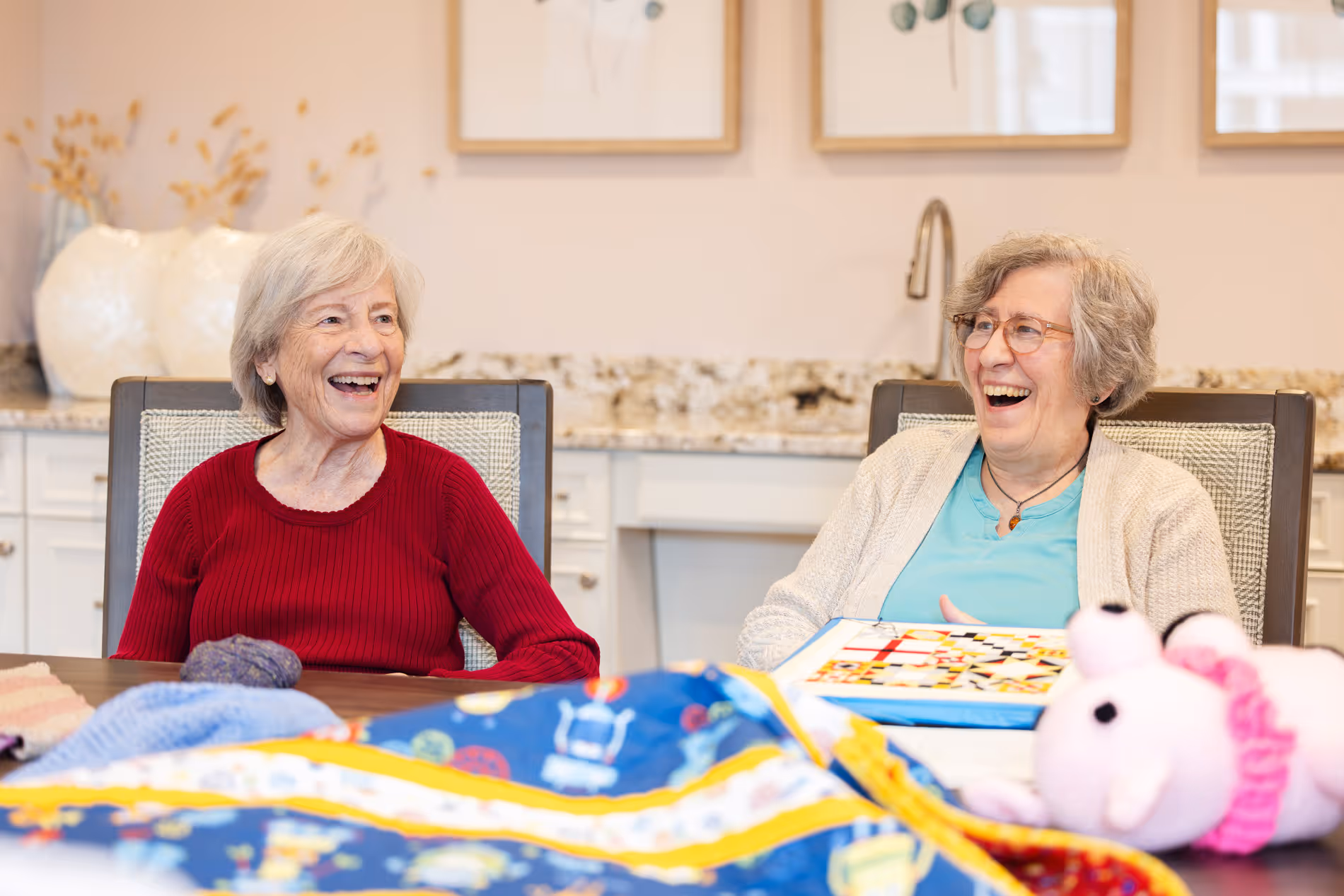 Two elderly women sitting at a table, smiling and laughing together.