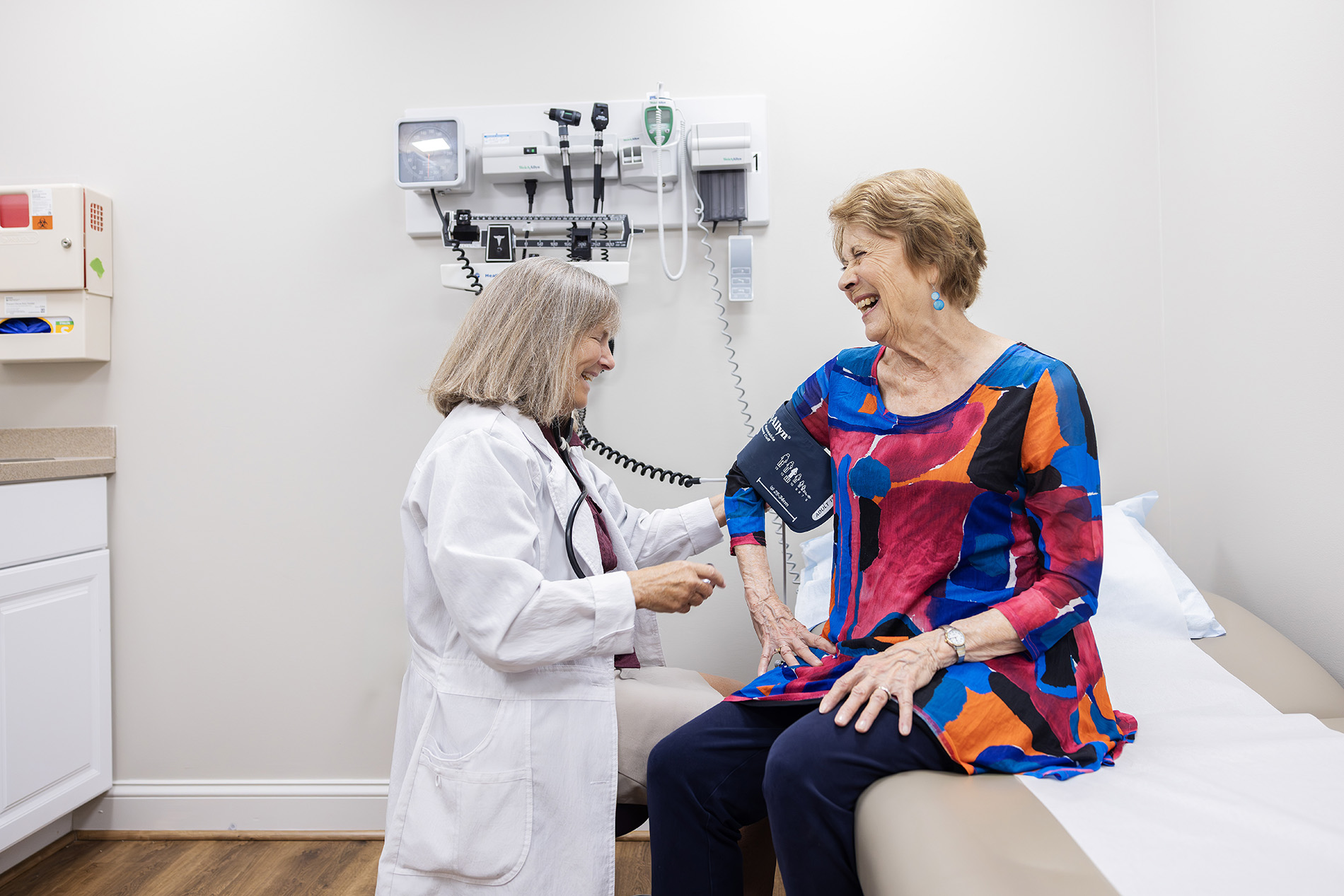 A doctor takes a woman's blood pressure in a medical examination room.