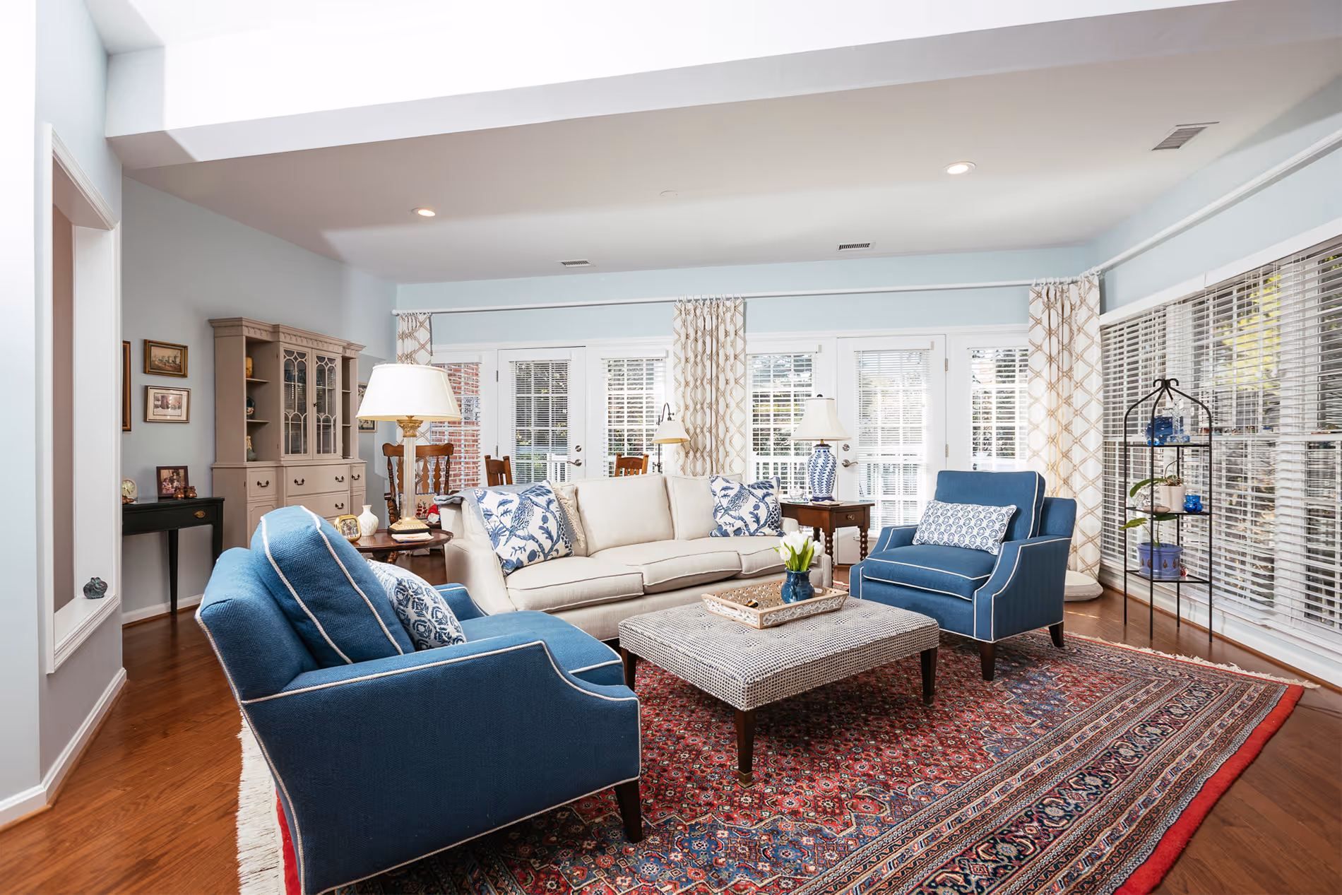 A living room with blue chairs, a beige sofa, a coffee table, and a patterned rug.