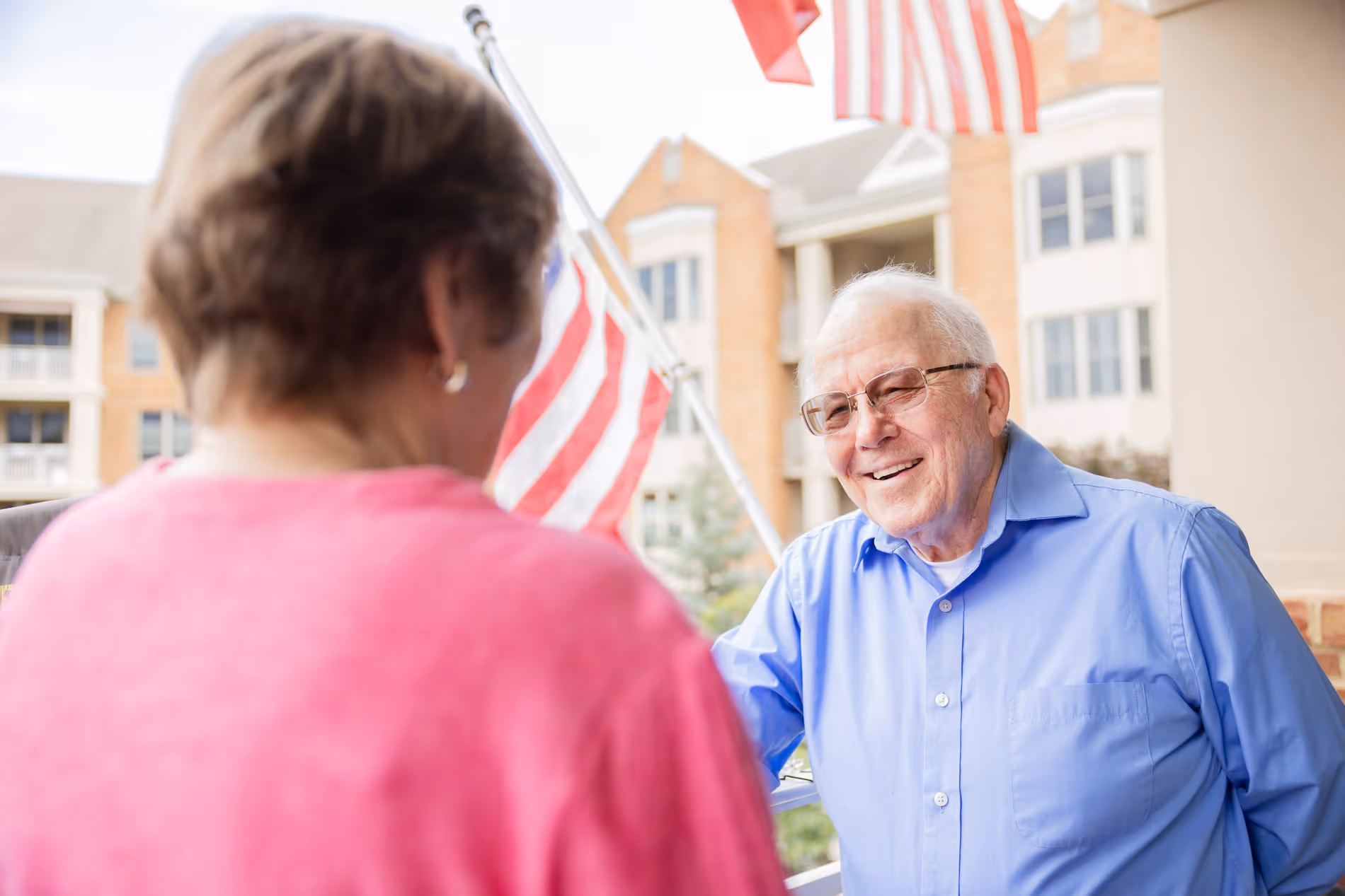 An elderly man in a blue shirt smiles while talking to a woman in a pink shirt.