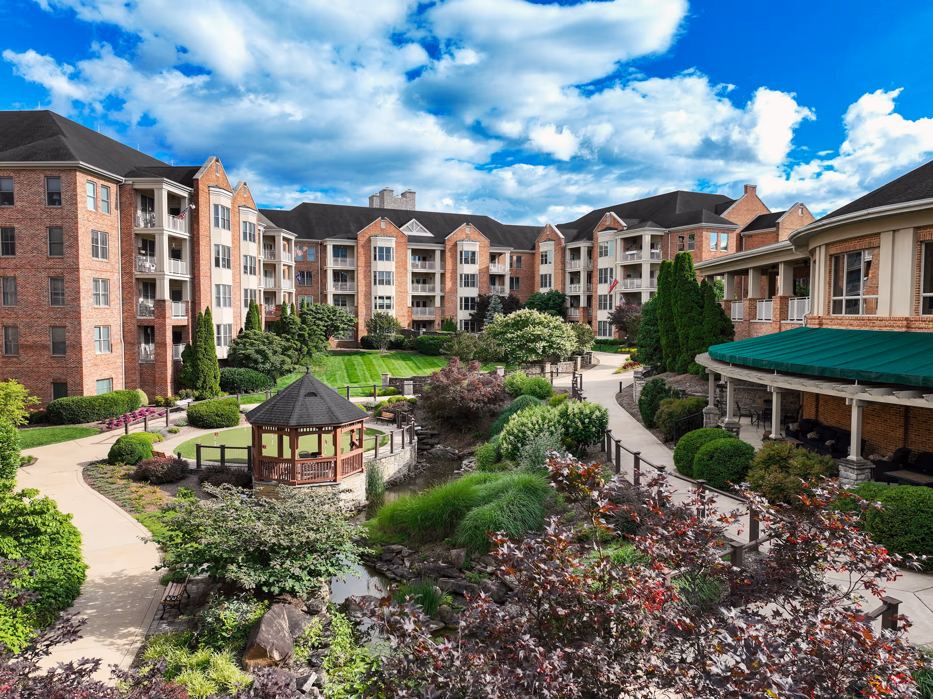 A courtyard with lush landscaping, pathways, and benches is surrounded by large residential buildings.