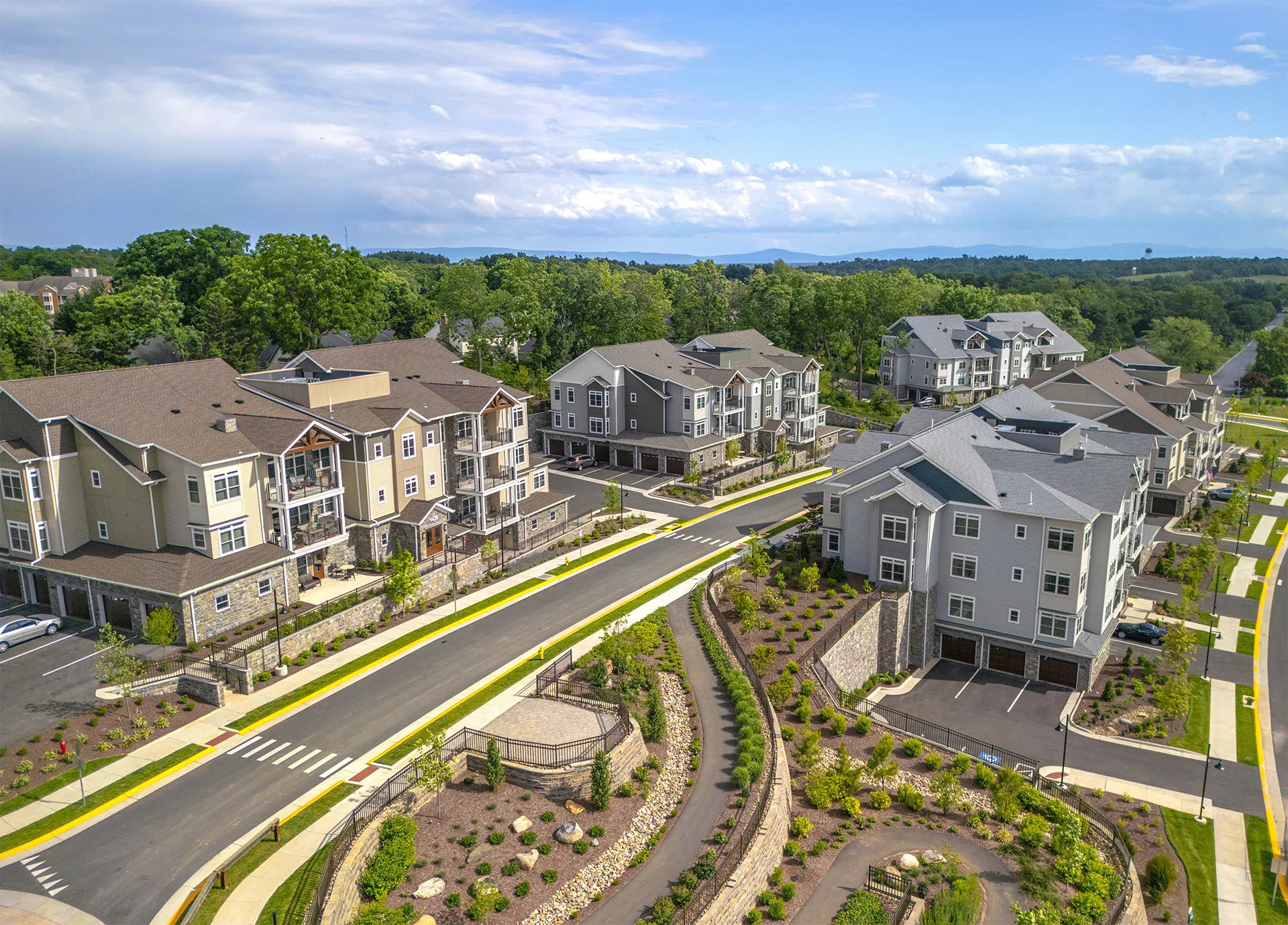 Aerial view of a suburban residential neighborhood with multi-story apartment buildings, landscaped paths, and a road running through.