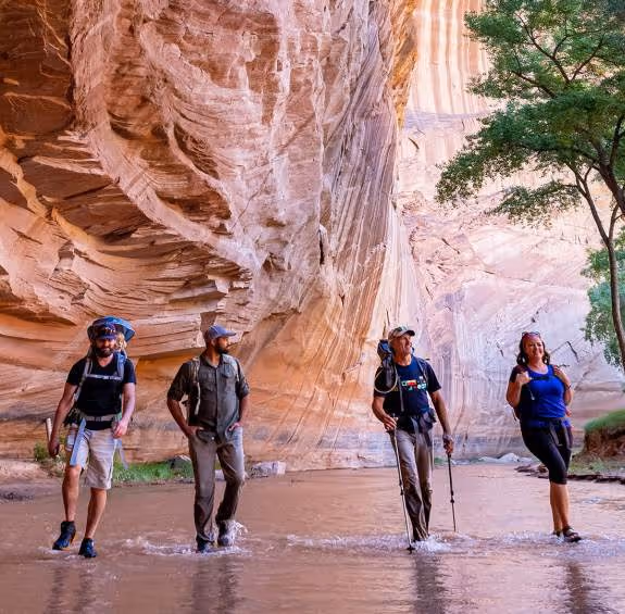 Hikers walking through water in a scenic red rock canyon with steep walls