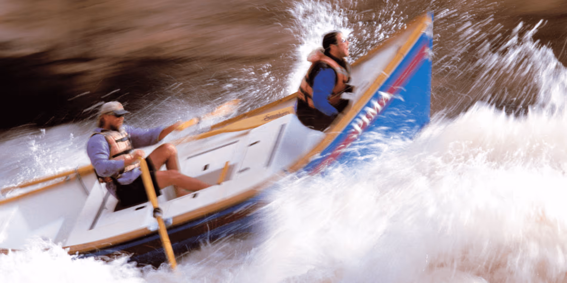 Two rafters navigating turbulent whitewater rapids with intense splashing